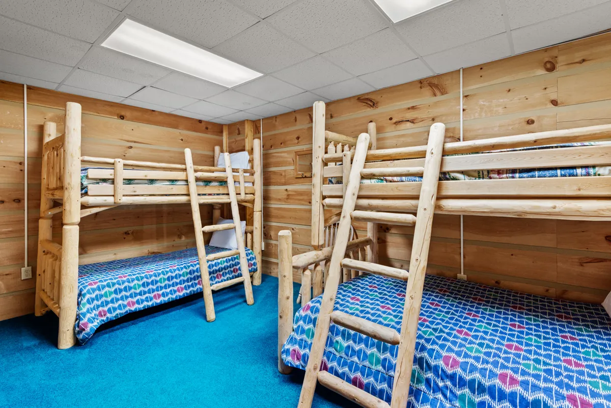 A cozy bunk room with wooden walls and playful, colorful bedding. The space is clearly designed with children or teens in mind, offering a fun and functional place for younger guests to relax or share bedtime stories.
