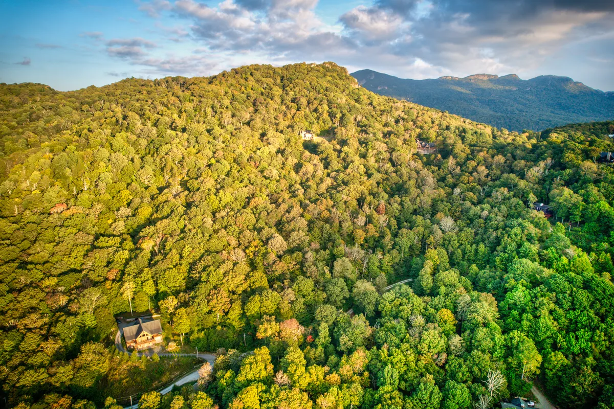 A panoramic view over a mountain range and dense forest, with an isolated house nestled in the landscape. This wide-angle shot situates the lodge within the grandeur of the Blue Ridge Mountains, evoking a sense of adventure and tranquility.