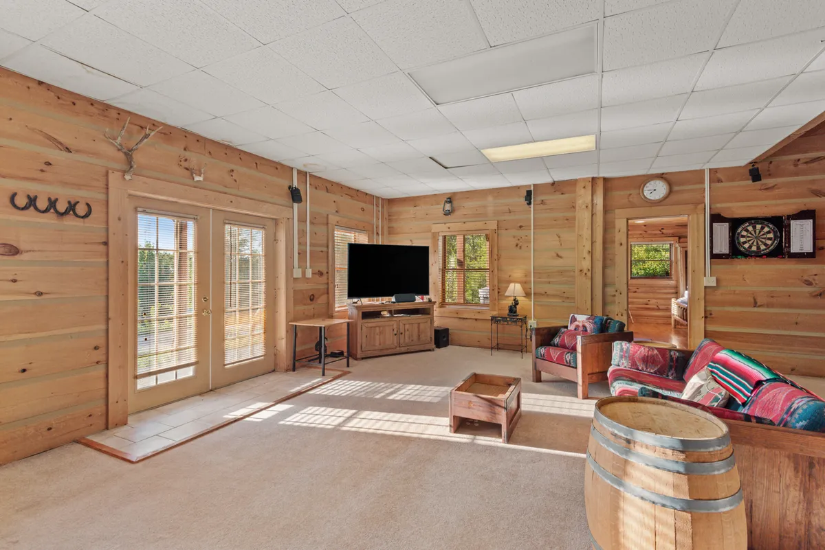 A comfortable, inviting entertainment den with a sofa, television, barrel table, and windows bringing in natural light. The space is designed for movie marathons, group relaxation, and casual gatherings.