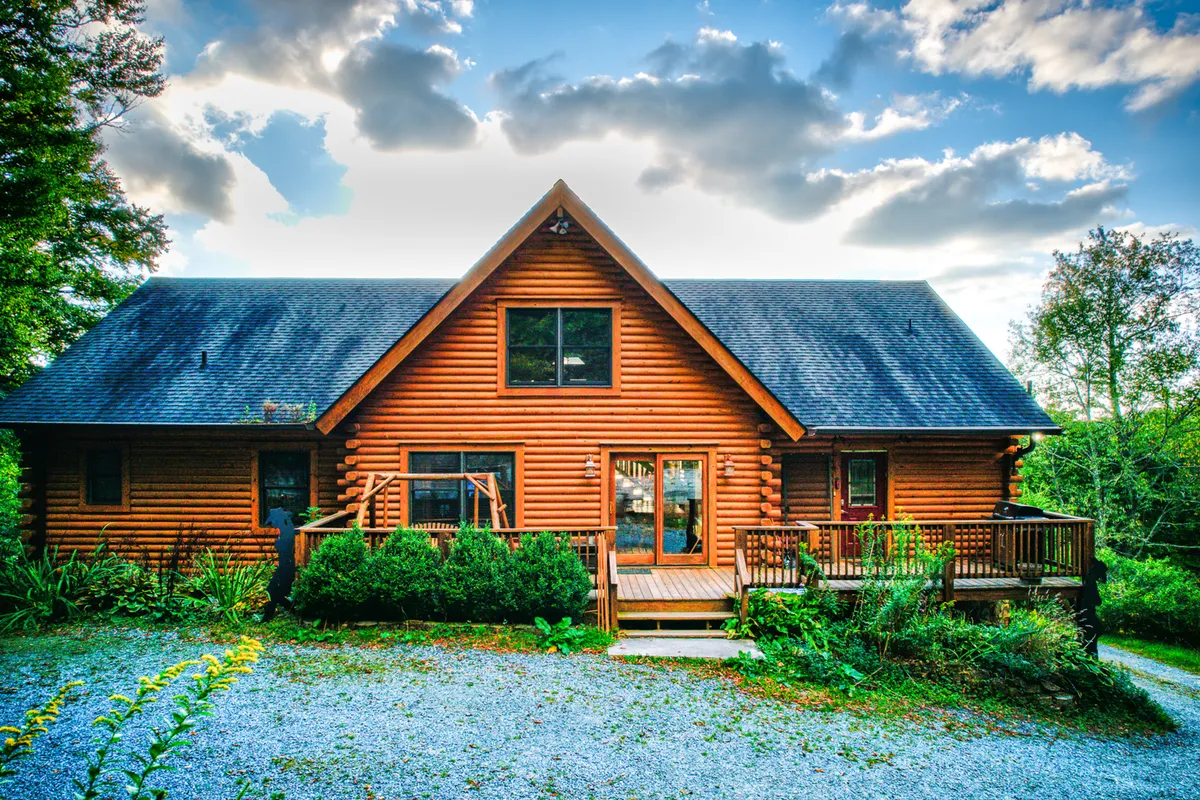 This image shows the exterior of Sugar Bear Lodge, featuring a welcoming log cabin structure with a spacious front porch surrounded by lush greenery. The inviting atmosphere hints at the possibility of outdoor gatherings and relaxation after a day of adventure.