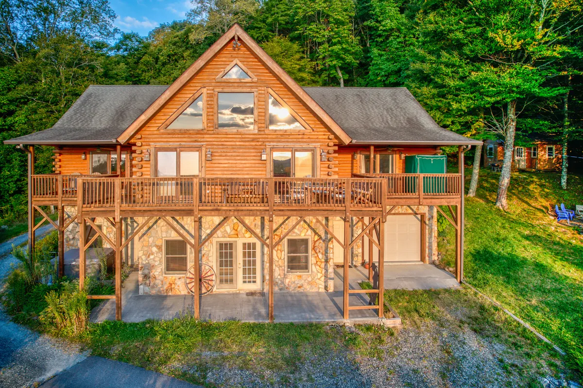 This image shows the inviting log cabin structure of Sugar Bear Lodge, featuring a large deck and a solid stone foundation surrounded by tall trees. The atmosphere is welcoming and hints at gatherings and relaxation just steps from nature. The spacious deck is ideal for après-ski hangouts or morning coffee before hitting the slopes.