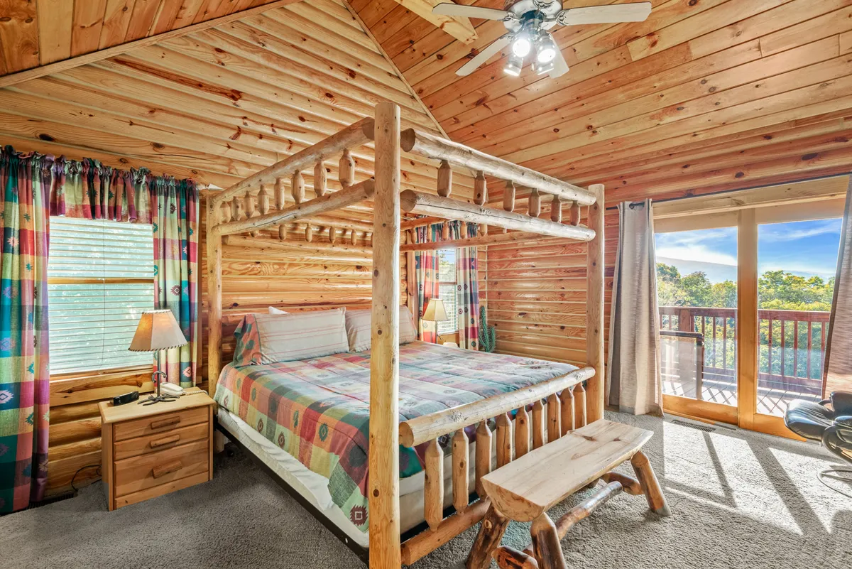 A spacious bedroom featuring a four-poster bed with plush bedding, warm wooden furniture, and large windows adorned with colorful curtains. The room is bathed in natural light, creating an inviting and tranquil atmosphere ideal for restful sleep.