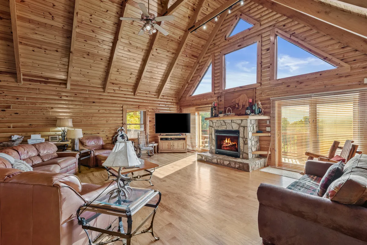 A cozy open-concept living room showcasing a roaring stone fireplace, comfortable seating arranged for conversation, and large windows framing stunning mountain vistas. The mood is warm, inviting, and ideal for group gatherings.